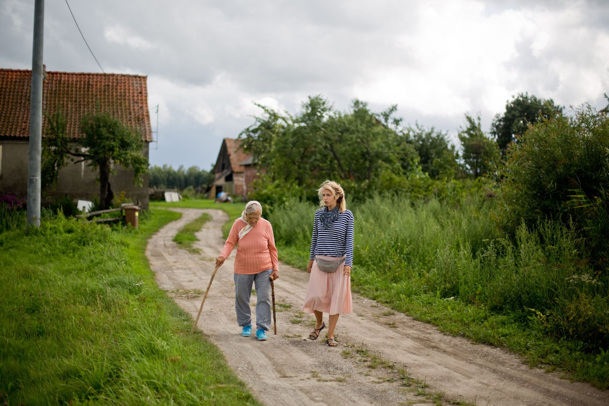 Fotografia (autor: Piotr Spigiel) przedstawia polną ścieżkę, prawdopodobnie prowadzącą do kilku widocznych w oddali domów. Na środku ilustracji uwiecznione zostały dwie kobiety idące w stronę fotografa, choć w ogóle nie zwracające na niego uwagi. Są zaaferowane rozmową. Jedna z postaci jest zdecydowanie starsza – to siwowłosa seniorka z założoną na głowę chustą, ubrana w sweter w kolorze łososiowym i szare, prawdopodobnie bawełniane spodnie. Idąc wspiera się dwiema laskami, ma lekko pochyloną głowę. Obok, może pół kroku przed nią, idzie młodsza kobieta – najprawdopodobniej autorka tekstu. Dziewczyna ma długie blond włosy, ubrana jest w pasiastą bluzę (biało- niebieską) oraz jasnoróżową spódnicę „za kolana”. Na stopach ma założone sandały. Obie kobiety są ubrane „letnio”. Choć aura – intensywna zieleń mijanych przez nie zarośli – podpowiada, że mogą być wakacje, to jednak ponad ich głowami niebo się zachmurza. Nie wiemy, czy za chwilę nie spadnie deszcz.